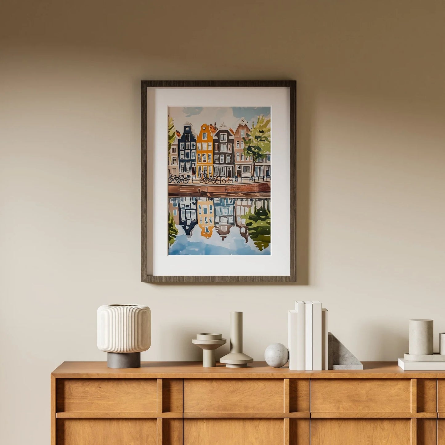 Framed artwork of a canal scene with houses on a beige wall above a wooden console table.