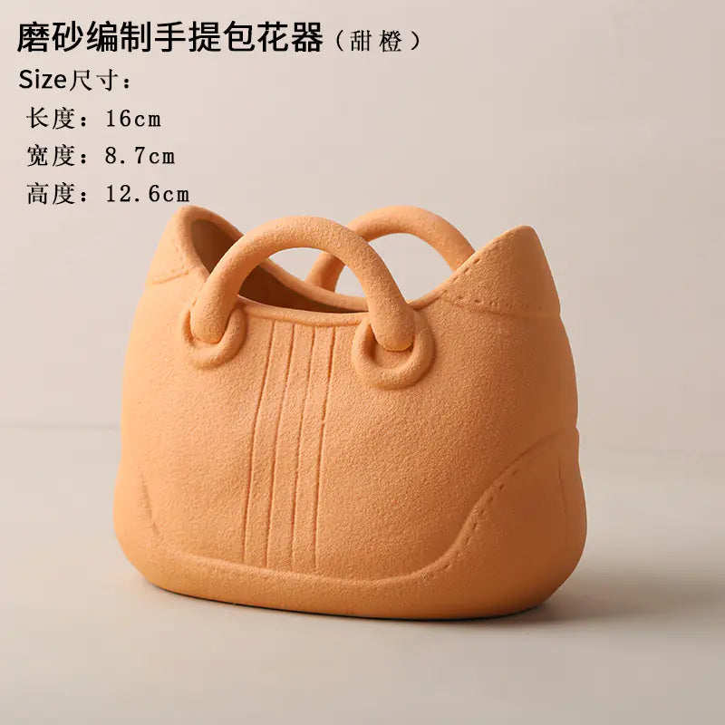 Orange handbag-shaped flower pot with handles on a beige background