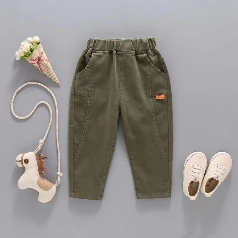 Green children's pants with a toy horse, flower cone, and shoes on a gray background