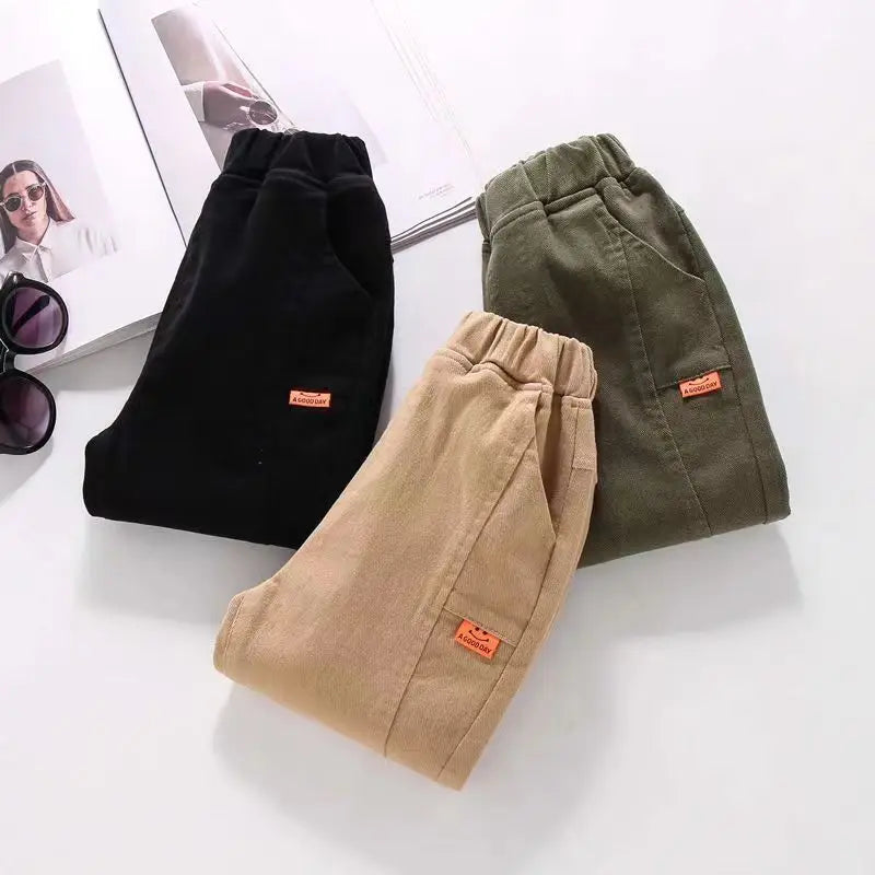 Three pairs of pants in black, beige, and green on a white surface with sunglasses and a magazine.
