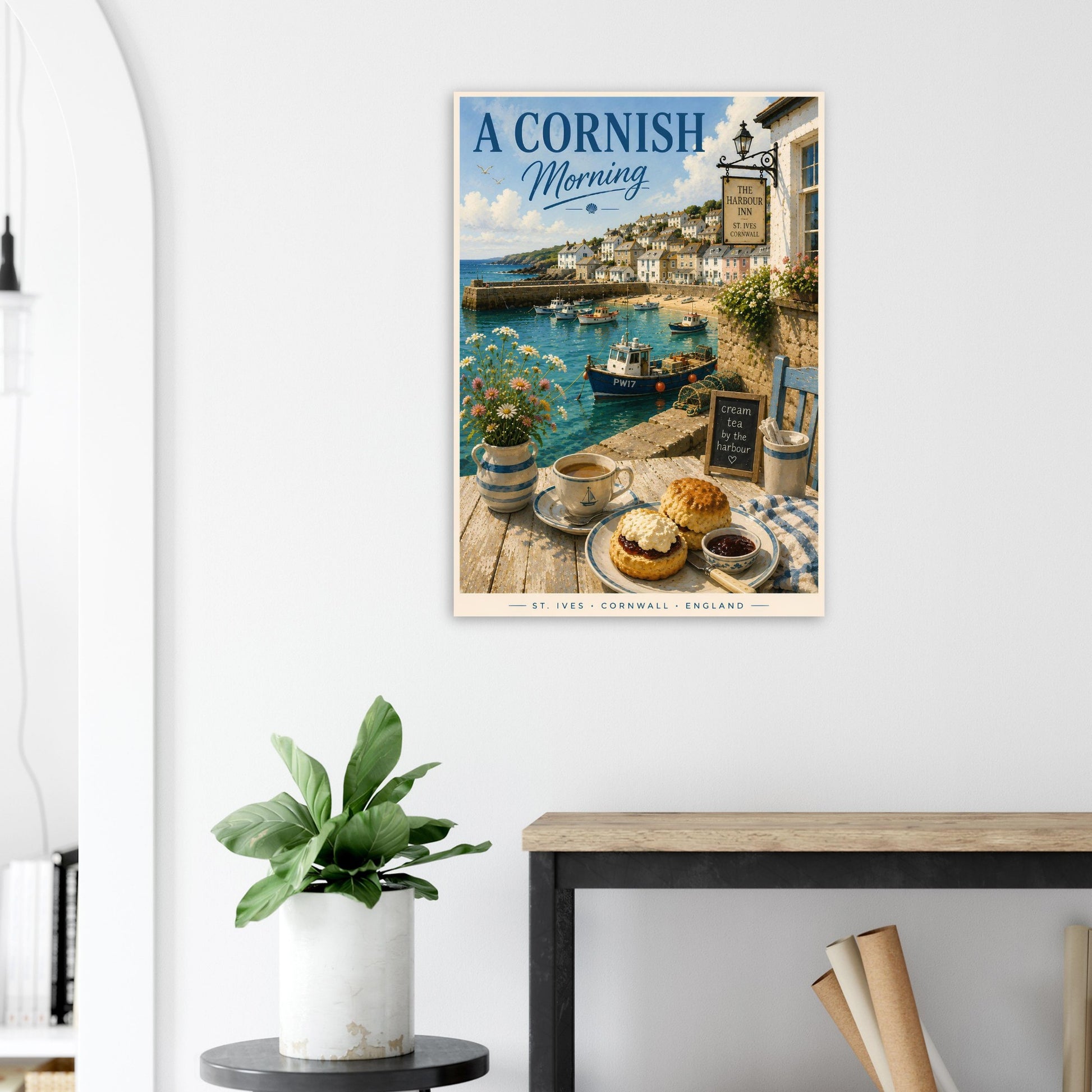 Framed artwork of a Cornish coastal scene with a table setting on a white wall.