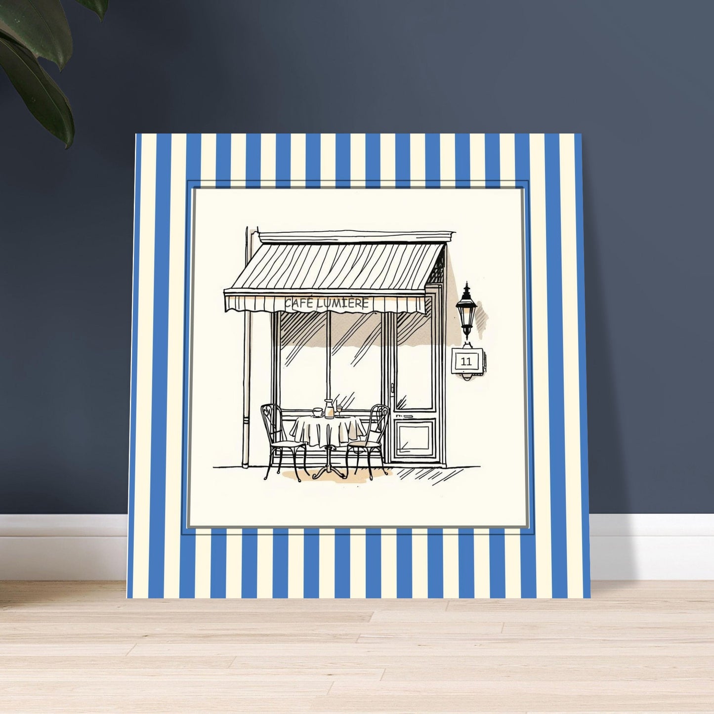 Square French café wall art print with blue striped border leaning against wall
