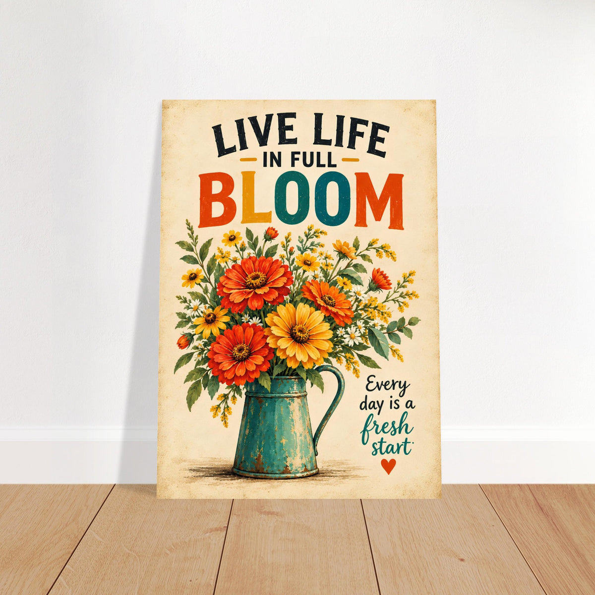 A vertical metal wall art print leaning against a white wall on a light wood floor. The print features a vintage-style illustration of a teal pitcher filled with red, orange, and yellow flowers, with the text 'LIVE LIFE IN FULL BLOOM' and 'Every day is a fresh start' on a warm beige background.