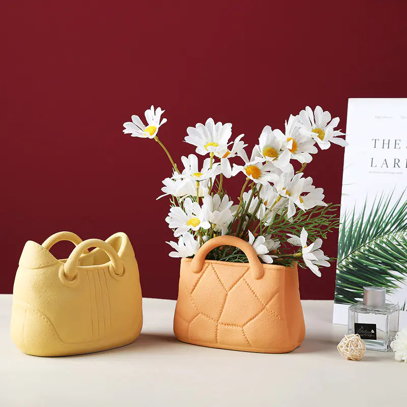 Two ceramic handbags with handles, one yellow and one orange, containing white flowers on a red background.