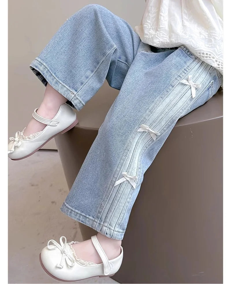 Light blue jeans with decorative bows and white shoes on a neutral background