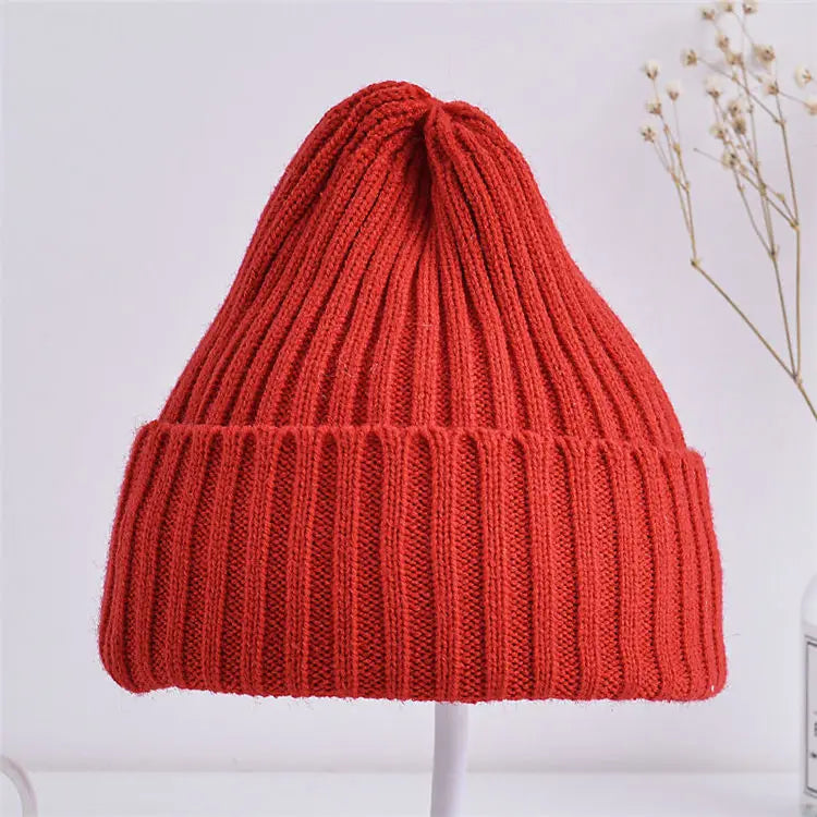 Red knitted beanie on a white stand with a light background
