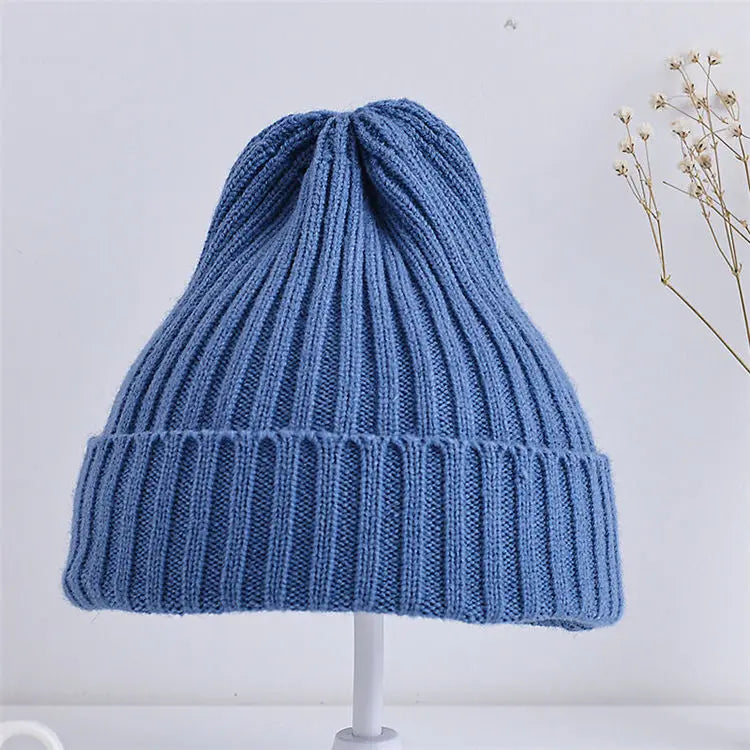 Blue knitted beanie on a white stand with a light gray background