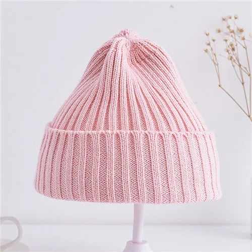 Pink knitted beanie on a white stand with a light gray background