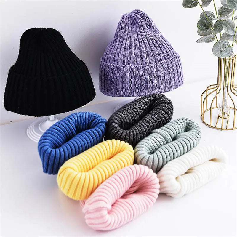 Collection of colorful knitted hats and scrunchies on a white surface with a decorative plant.
