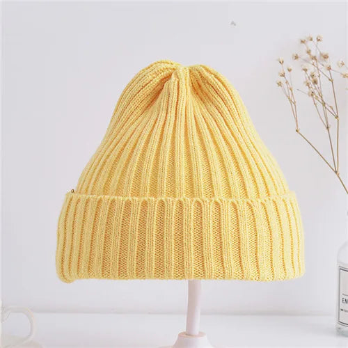 Yellow knitted beanie on a white stand with a light background