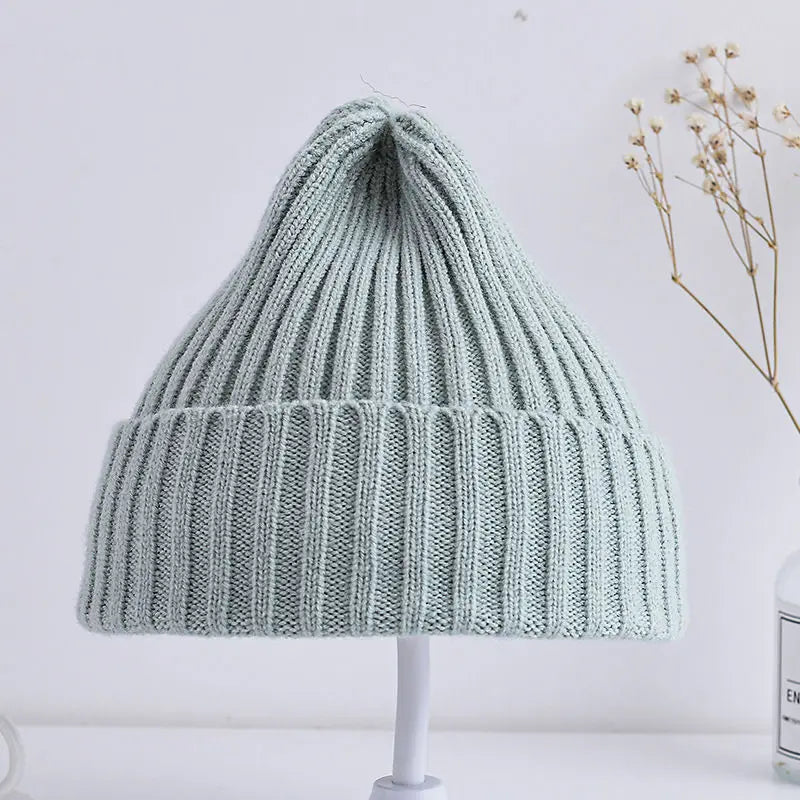 Light green knitted beanie on a white stand with a minimal background