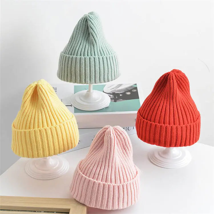 Four colorful knit beanie hats on white stands against a light gray background.