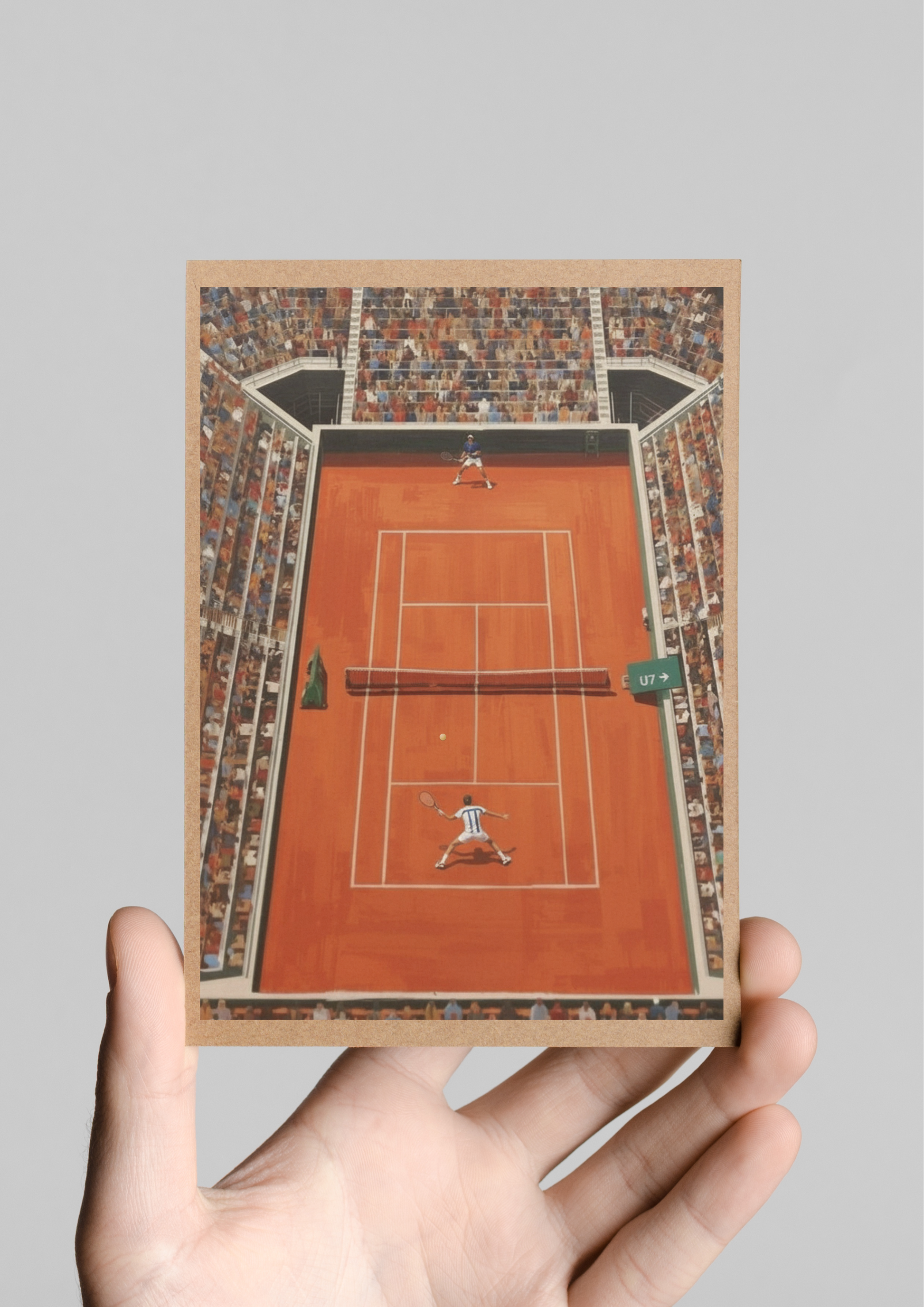 Hand holding a card with a miniature tennis court design on a gray background