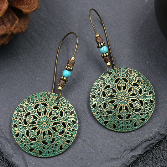 Pair of green and gold lace-style earrings on a dark stone surface
