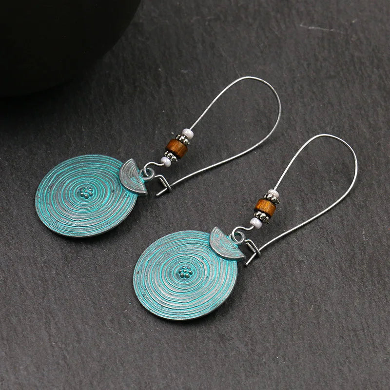 Pair of turquoise circular earrings with silver and brown accents on a dark surface