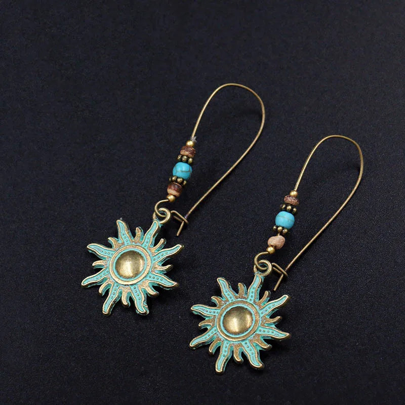 Sun-shaped earrings with turquoise and gold details on a black background