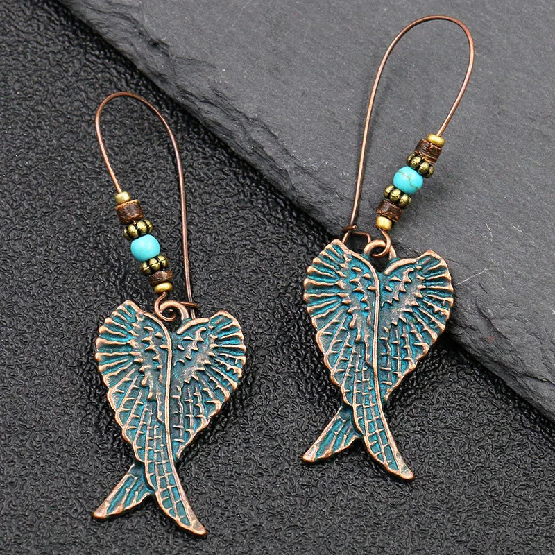 Pair of angel wing earrings with turquoise accents on a dark stone surface