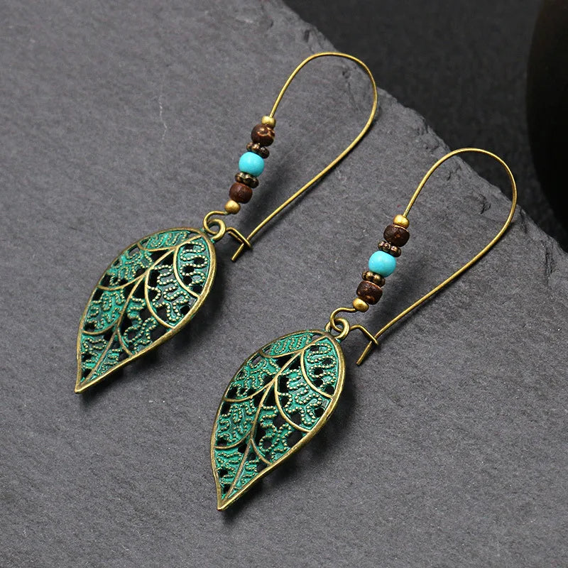 Pair of green leaf-shaped earrings with gold accents on a dark stone surface