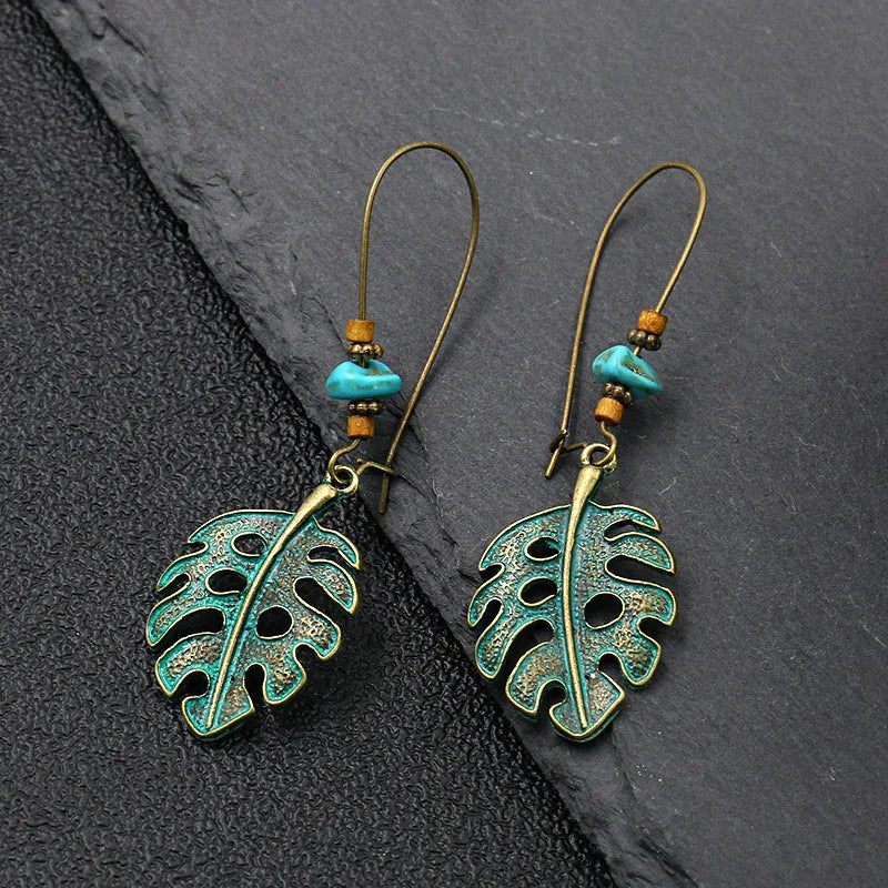 Pair of leaf-shaped earrings with turquoise beads on a dark stone surface