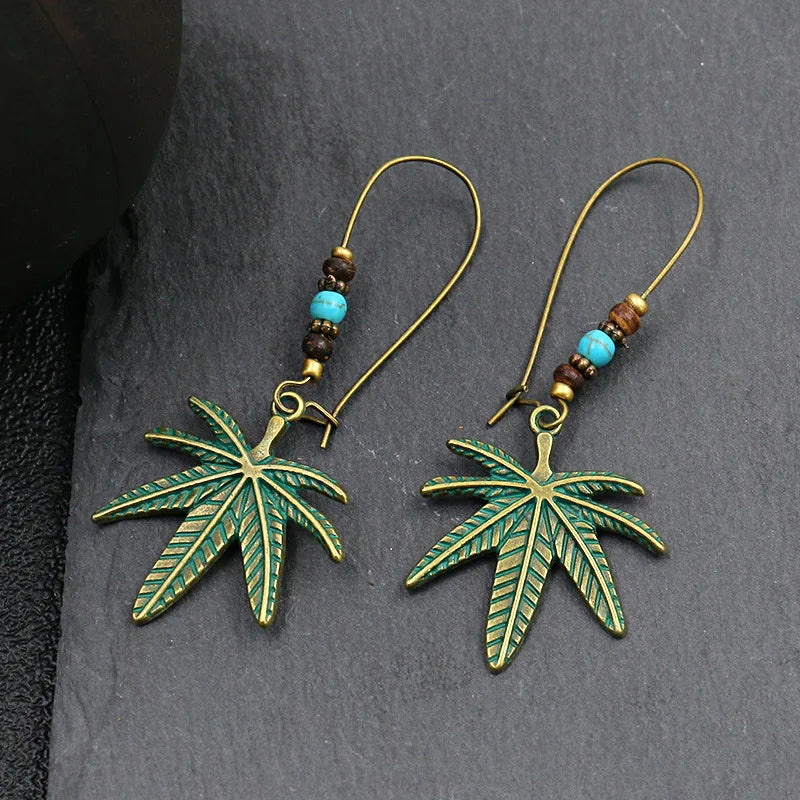 Bronze cannabis leaf earrings with turquoise and brown beads on a dark surface