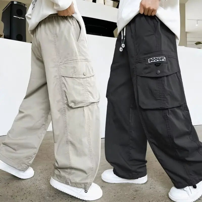 Two pairs of cargo pants, one grey and one black with a brand logo, worn by people indoors.