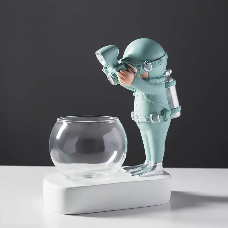 Figurine of an astronaut holding a camera next to a glass bowl on a dark background
