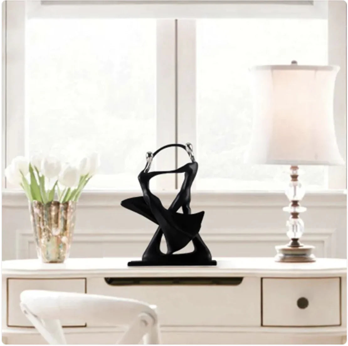 Black abstract sculpture on a white surface with a lamp and plant in the background