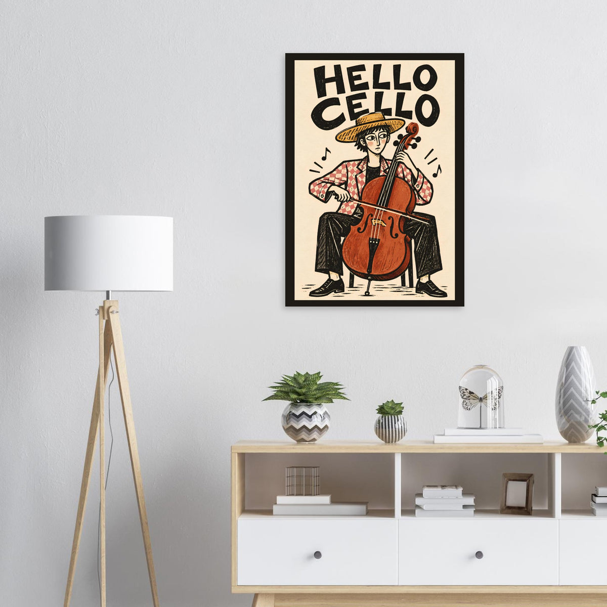 A framed retro-style poster featuring an illustration of a cellist with the text 'HELLO CELLO' hangs on a light gray wall above a white cabinet with decorative plants and objects. A floor lamp stands to the left.