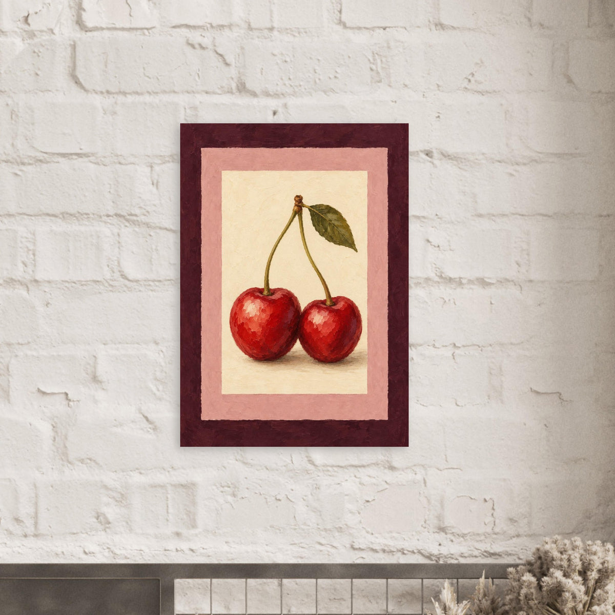 A framed art print featuring a still life of two red cherries with green leaves, displayed on a white brick wall.