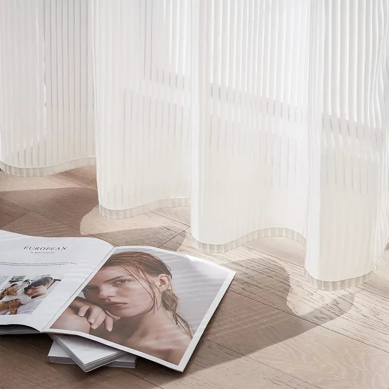 Open magazine on a wooden floor with sheer white curtains in the background