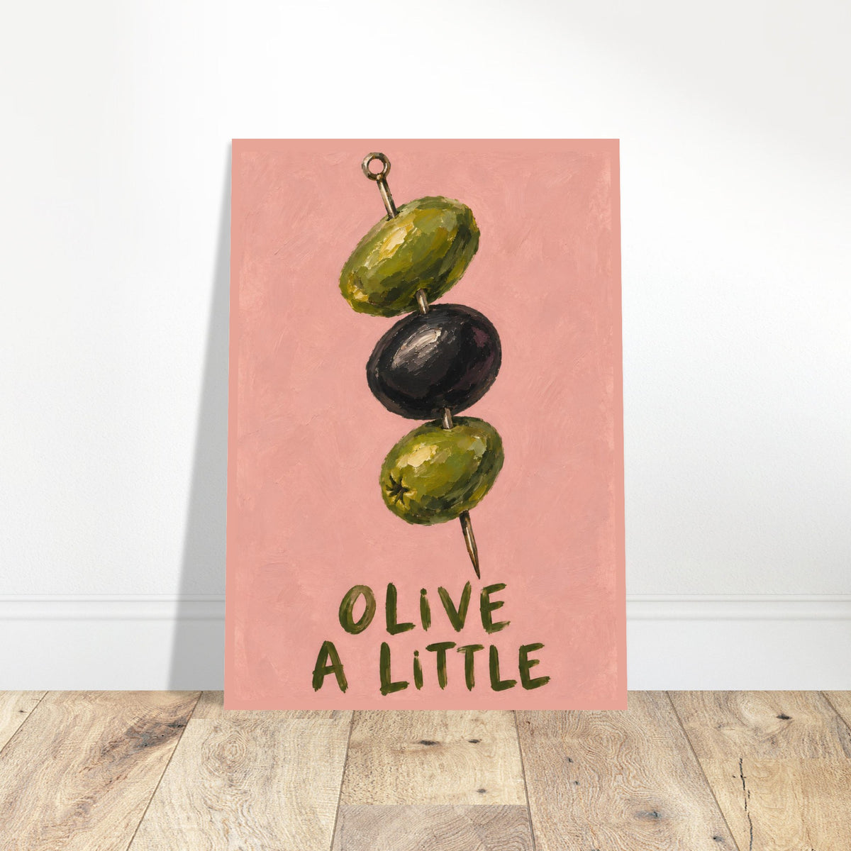 Unframed Olive a Little print resting on a wooden floor against a white wall.