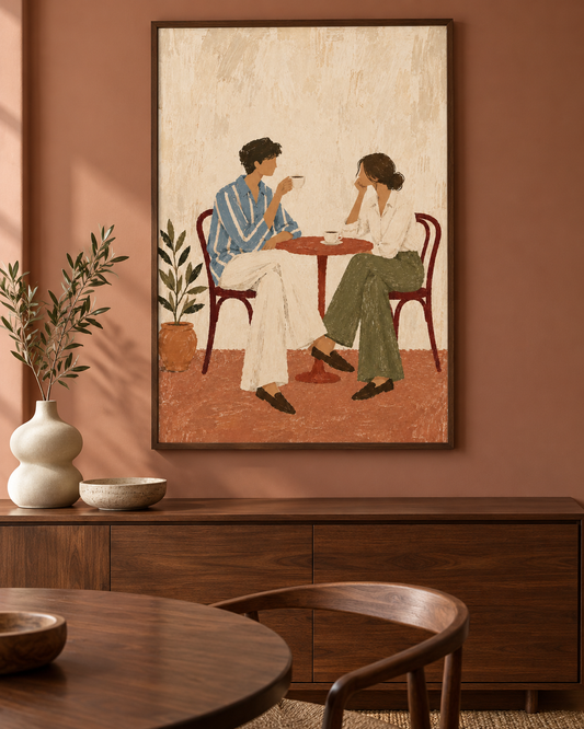 A framed art print depicting a couple sitting at a small table, displayed on a terracotta-colored wall above a wooden sideboard in a styled room.