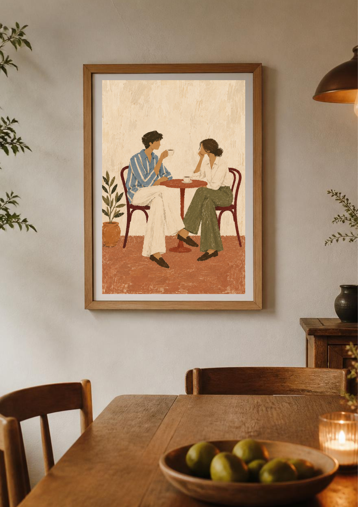 A framed art print depicting a couple sitting at a table, hanging on a light gray wall above a wooden dining table with a bowl of green fruit in the foreground.