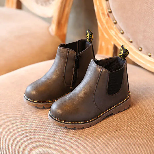 Pair of brown children's boots with black accents on a beige surface.