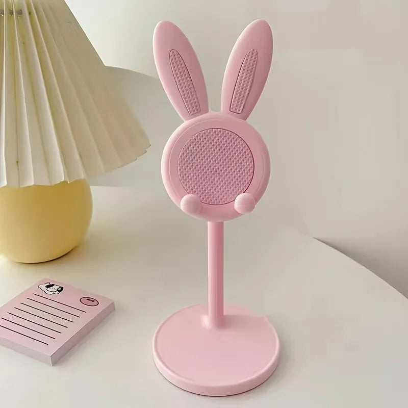 Pink bunny-shaped phone stand on a white surface with a lamp in the background