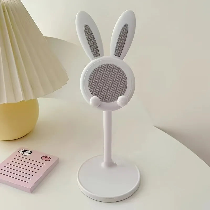 White microphone with bunny ears on a stand next to a pink notepad on a light surface.
