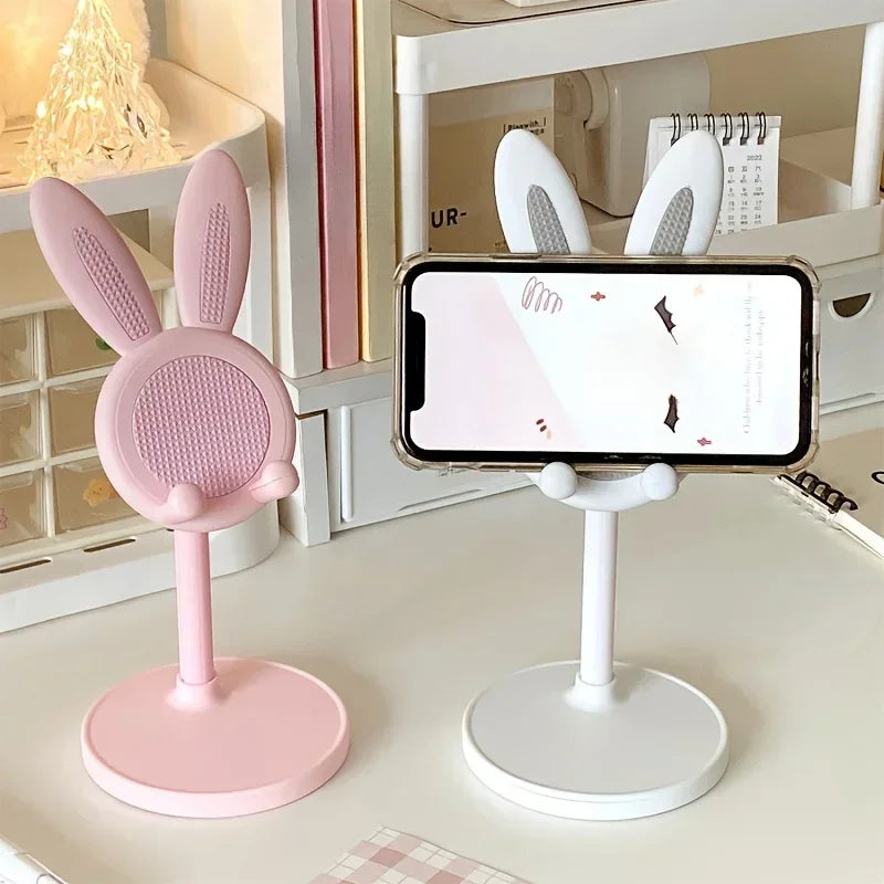 Pink bunny-shaped phone stand next to a white stand with a phone on a desk.