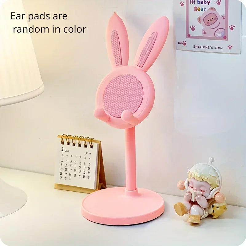 Pink bunny-shaped phone stand on a desk with a calendar and small figurine in the background.