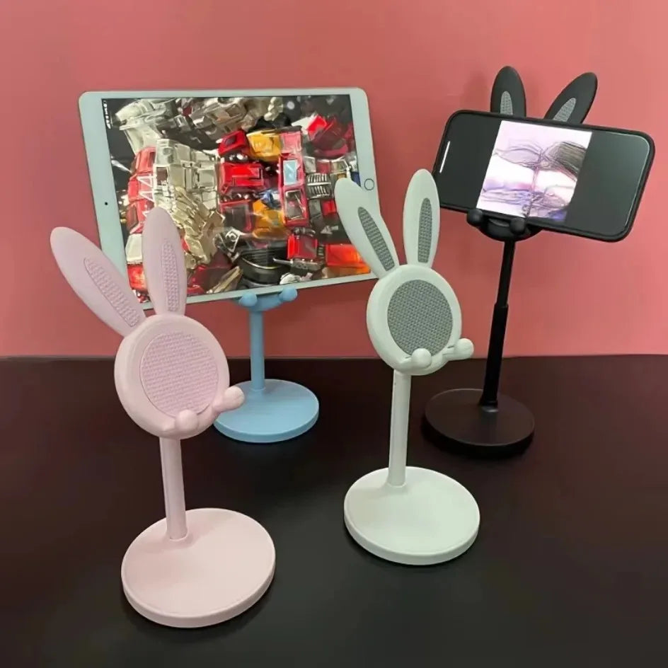 Three phone stands with bunny ears on a dark surface against a pink background