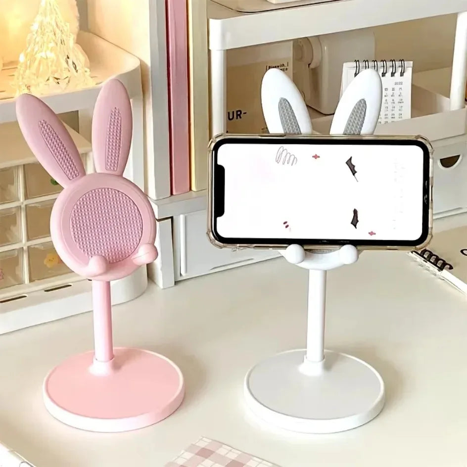 Pink bunny-shaped phone stand next to a white phone stand on a desk.