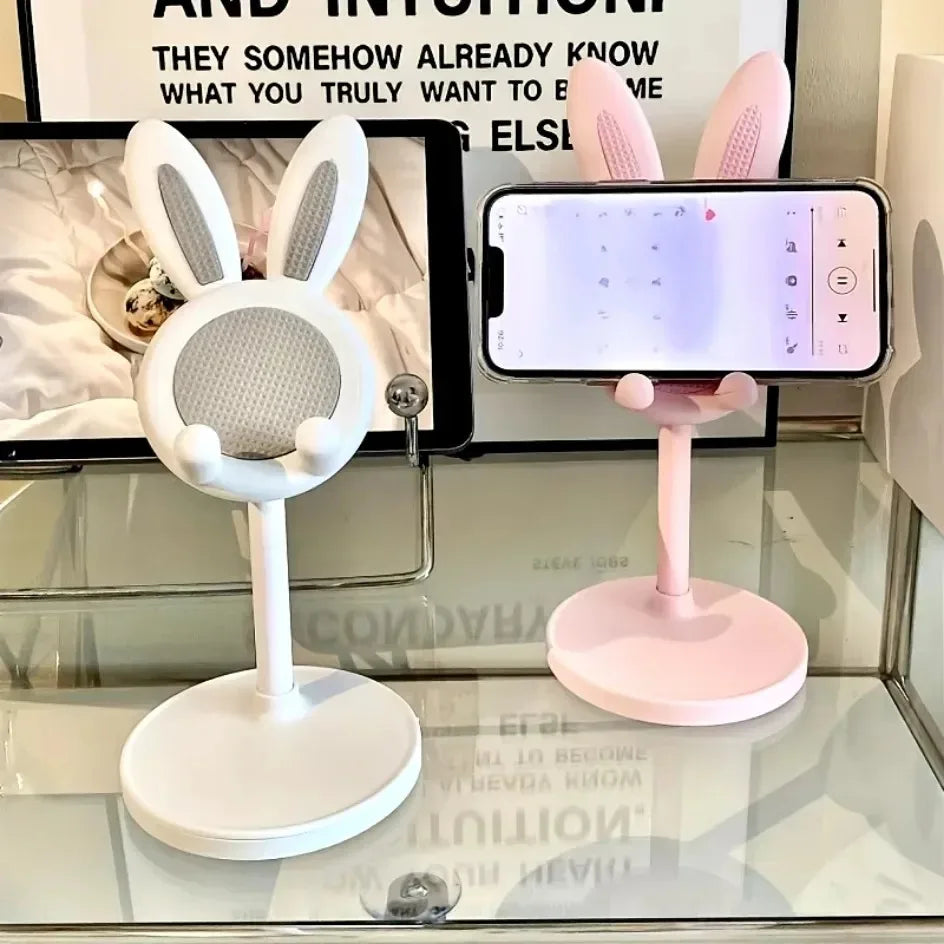 Two phone stands with bunny ears, one white and one pink, on a reflective surface.