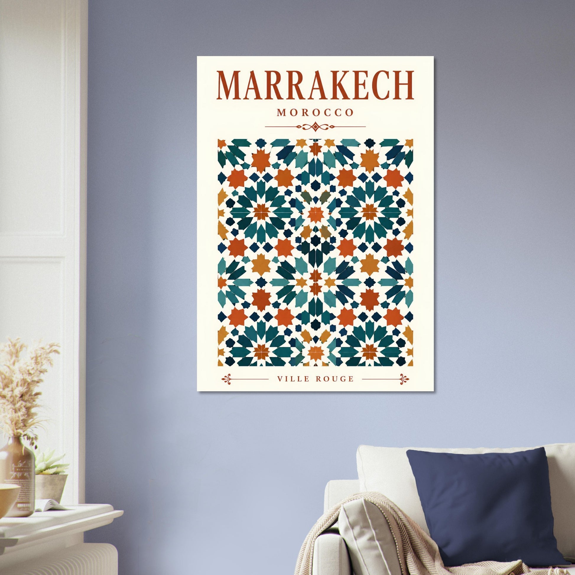 A vertical travel poster of Marrakech, Morocco, featuring a colorful Moroccan tile pattern, displayed on a light blue-gray wall above a sofa in a living room setting.