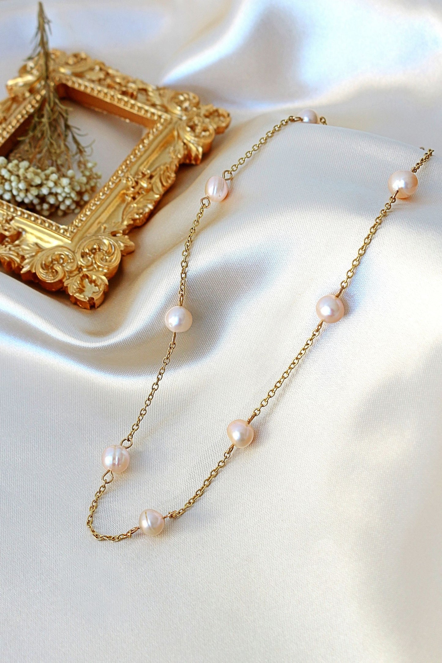 Pearl necklace with gold chain on a white surface with a decorative frame in the background.