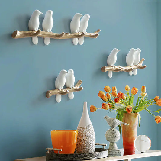 Decorative wall art with birds on branches against a blue wall, with a table displaying vases and flowers.