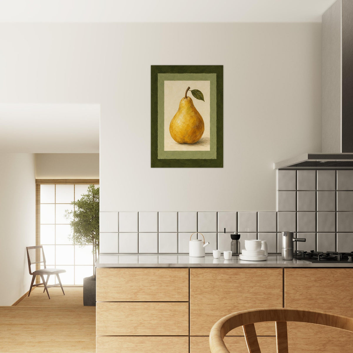 A framed art print of a yellow pear with a green leaf, displayed on a white wall above a modern kitchen with light wood cabinets and white tiles.