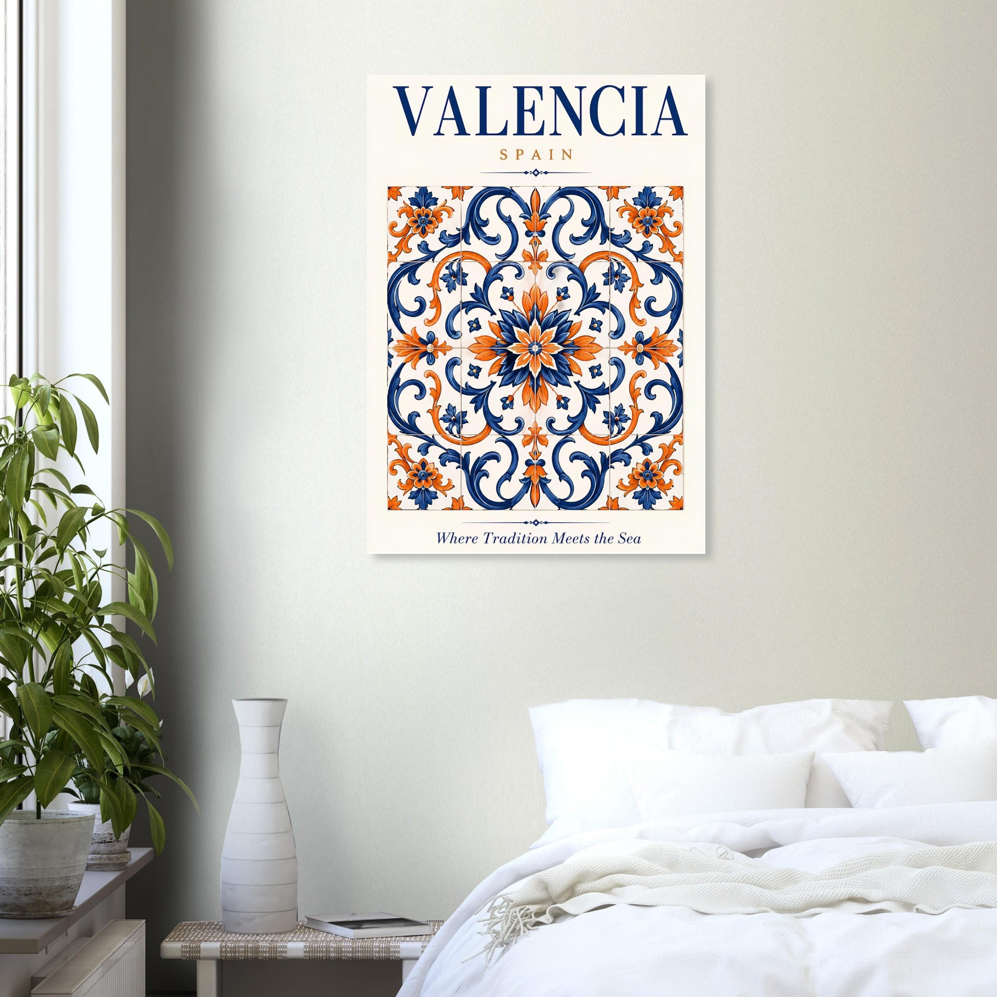 A framed wall art print featuring a decorative tile pattern with the text 'VALENCIA SPAIN' and 'Where Tradition Meets the Sea,' displayed above a bed in a bright bedroom with a plant and vase.
