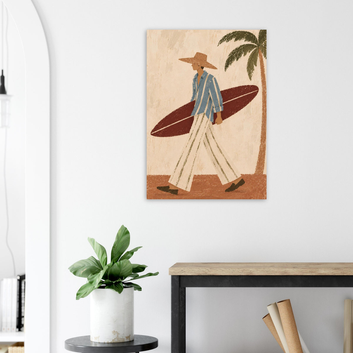 Unframed surfer poster on a light wall above a console table, styled with a small green plant and leaning frames.