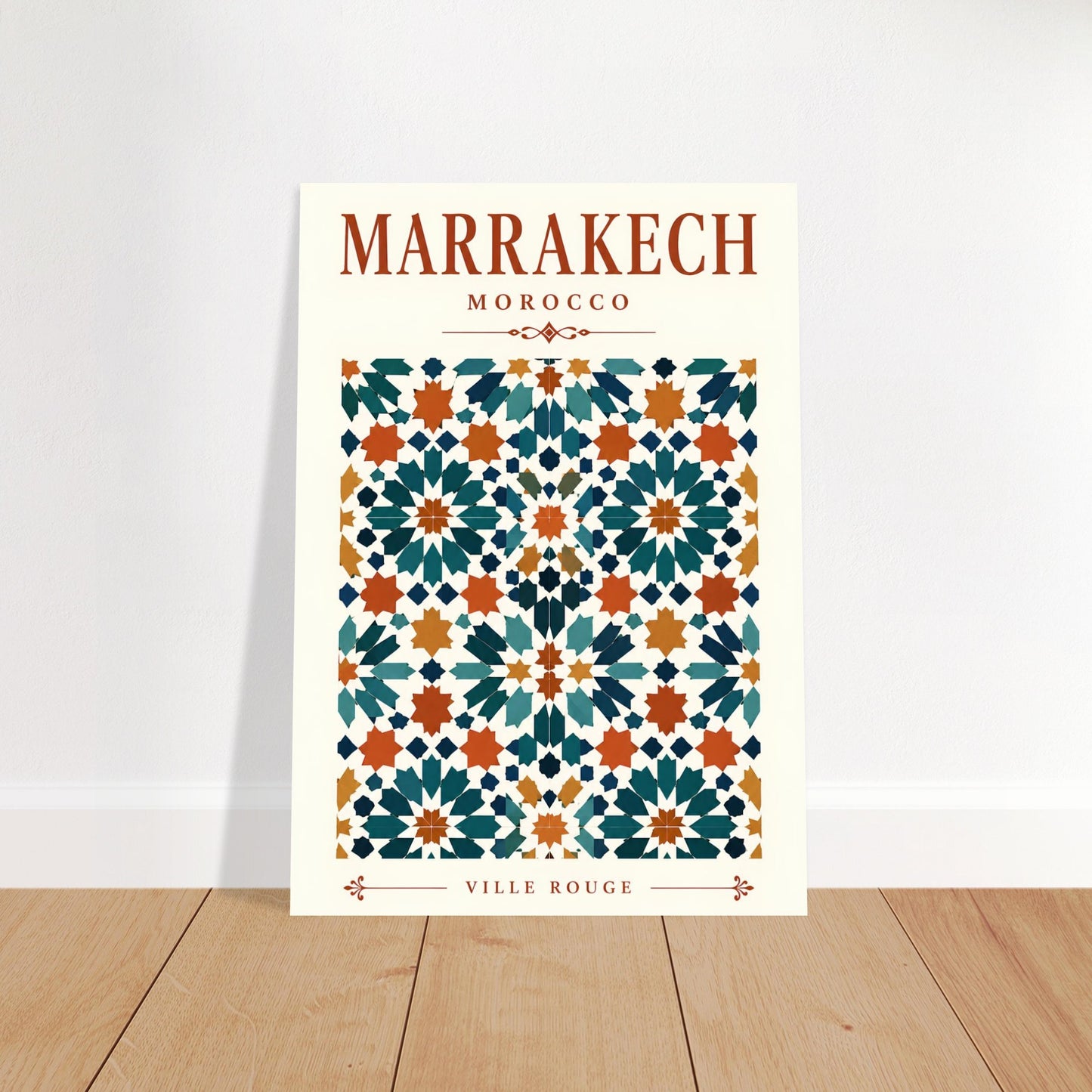 A vertical art print featuring a Moroccan tile pattern with the text 'MARRAKECH MOROCCO' at the top and 'VILLE ROUGE' at the bottom, leaning against a white wall on a light wood floor.