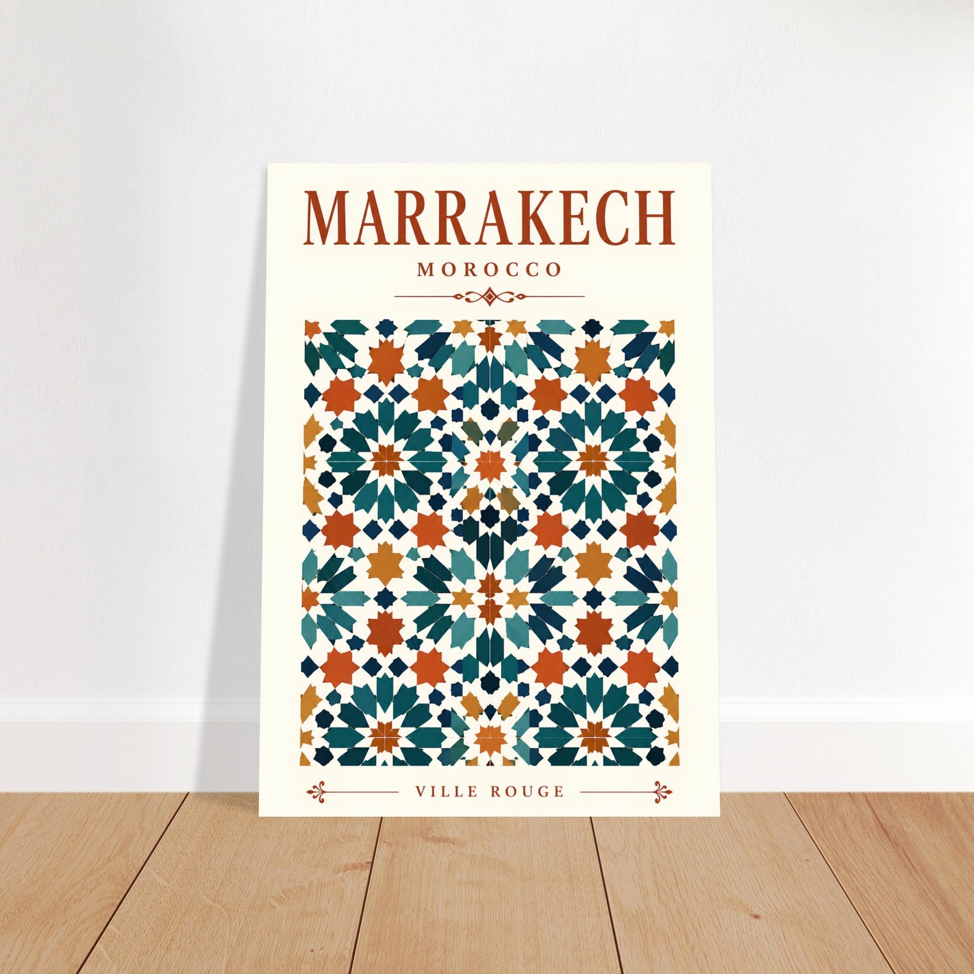 A vertical art print featuring a Moroccan tile pattern with the text 'MARRAKECH MOROCCO' at the top and 'VILLE ROUGE' at the bottom, leaning against a white wall on a light wood floor.