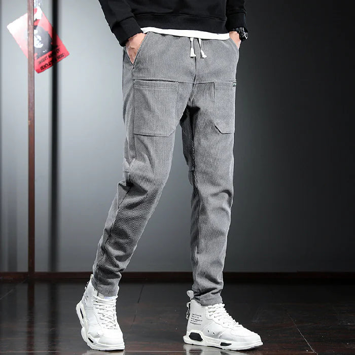 Person wearing gray cargo jogger pants with a black top and white sneakers on a dark background